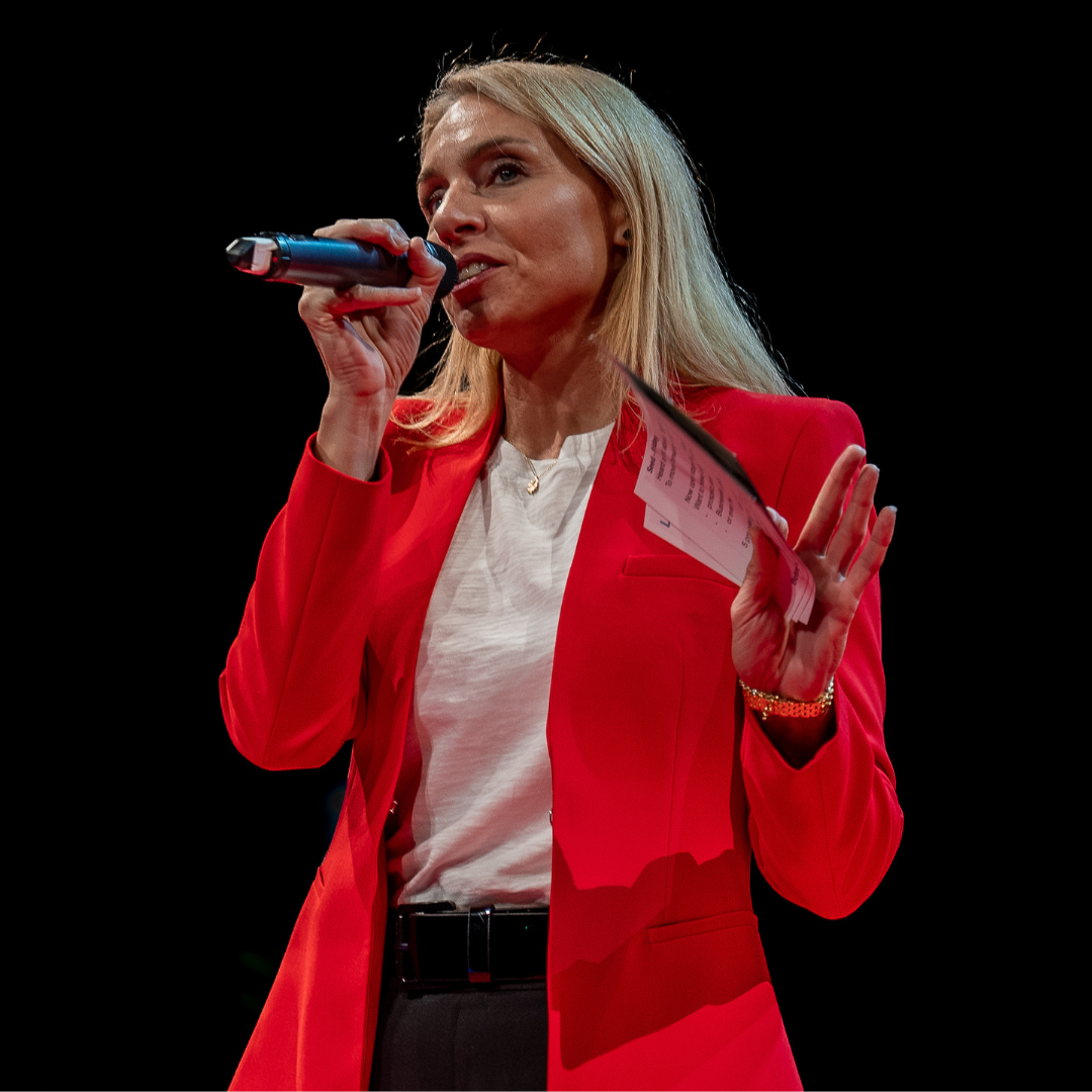 Blazy Flash speaking into a microphone on stage in a red jacket