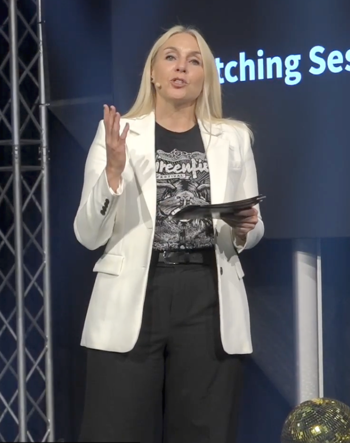 Blazy Flash speaking on stage in a white jacket with a headset microphone